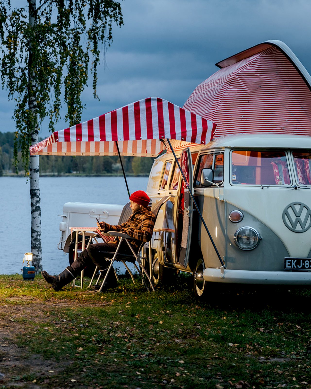 Karavaanari viettää iltaa Volkswagen Kleinbusin edessä järven rannalla.