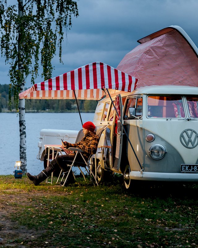 Karavaanari viettää iltaa Volkswagen Kleinbusin edessä järven rannalla.