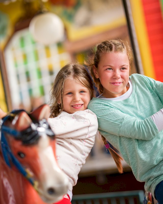 Kaksi tyttöä poseeraa karusellin kyydissä.
